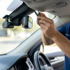 لقطة مقربة ملتقطة من داخل مركبة تُظهر يد فني في الرياض وهي تقوم بعناية بدس سلك أسود رفيع لكاميرا لوحة القيادة (داش كام) المثبتة حديثًا داخل تنجيد سقف السيارة، بجوار مرآة الرؤية الخلفية.