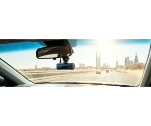 مشهد بانورامي من داخل سيارة يوضح داش كام بمكثف فائق مثبتة خلف مرآة الرؤية الخلفية، تطل على طريق سريع مشمس في الرياض مع تموجات حرارية ظاهرة فوق الأسفلت الساخن في صيف السعودية.